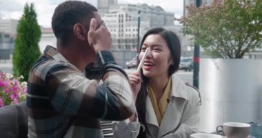 Elleriyle gözlerini kapatan bir adamın arkadan görünüşü sonra sevgilisinin pozitif hamilelik testine bakıp güzel güneşli bir günde romantik bir kafede ona nazikçe sarılıyor.