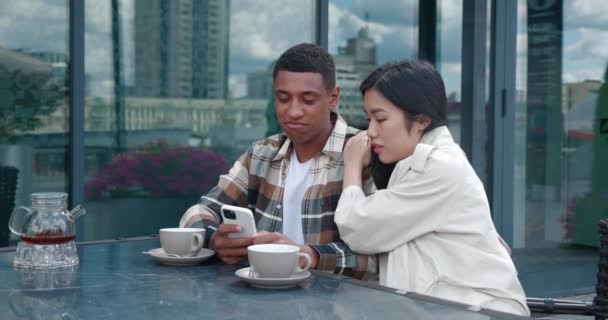 Young woman consoles her friend feeling frustrated after reading the worst news on a cell phone while sitting together in the rooftop on an outdoor cafeteria. Focus on emotions of desperation, support — Stock Video