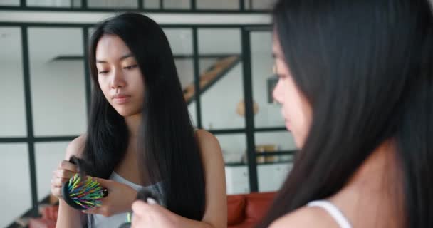 Attraente donna asiatica pettinare i capelli con una spazzola per capelli, guardando il suo riflesso specchio, ed esaminando attentamente le estremità dei capelli. Concetto di cura del corpo e della salute, igiene e bellezza del mattino. — Video Stock