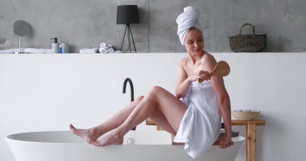 Magnifique femme blonde avec les yeux fermés dans le plaisir enveloppé dans une serviette éponge de bain blanche, masse ses épaules, le dos et les mains, effectuant un traitement du corps lissant avant de prendre un bain moussant relaxant. — Video