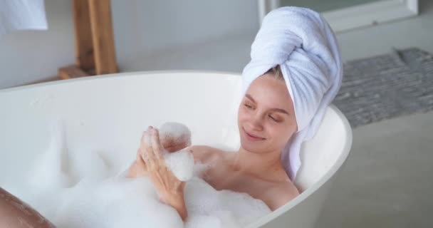 Detailní záběr veselé ženy, jak se doma povaluje v koupelně, koupe se v bublině, myje si tělo, stará se o kůži, usmívá se zubatým úsměvem, zatímco si hraje s mýdlovou pěnou. Home SPA a koncepce čistoty — Stock video