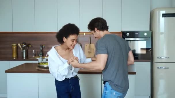 Romántica pareja diversa bailando en la cocina. Dos personas felices, hombre caucásico y mujer afroamericana disfrutando de divertidos momentos juntos en casa — Vídeos de Stock