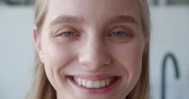 Güzel gülüşü olan ve kameraya bakan çekici genç bir kadının kırpılmış görüntüsü. Uzun sarı saçlı neşeli bir kadının yakın plan yüz portresi. Sevinçle gülüyor, banyo arkasında poz veriyor.