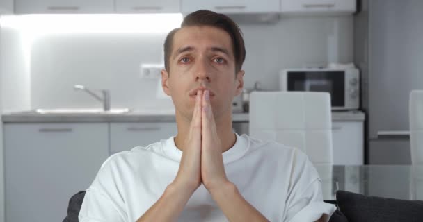Грустный человек со слезами на глазах просит помощи о проблеме, молится Богу. Религиозный мужчина сидит дома на диване и молится. Парень молится с надеждой. — стоковое видео