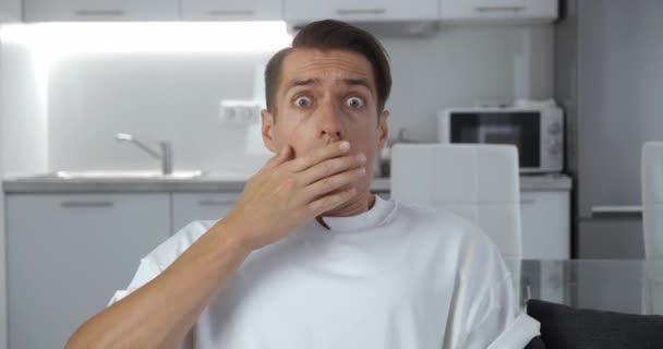 Close-up portrait of scared man bulging eyes and covering mouth in fright reacting on horrible situation on home office apartment background — Stock Video