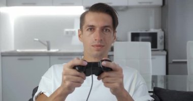 Oturma odasında kanepede otururken bilgisayar oyunu oynayan mutlu bir oyuncu. Genç, gülümseyen bir erkek video oyununda sevinçten havalara uçuyor.