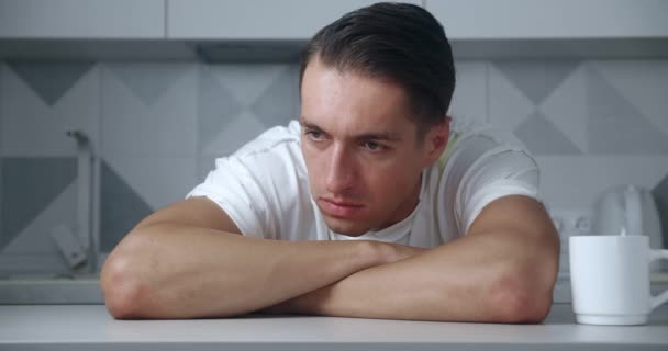 Портрет беспокойного и напряженного молодого человека, сидящего за столом дома. Депрессивный мужчина, страдающий от горя или неудачи — стоковое видео