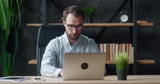 Сконцентрированный человек-фрилансер в очках, работающий на ноутбуке на современном рабочем месте, дистанционно дома. Мужчина-предприниматель с помощью компьютера, чаты в социальной сети, печатные сообщения, интернет-серфинг. — стоковое видео