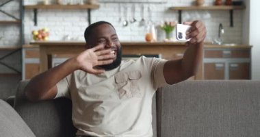 Genç ve yakışıklı Afro-Amerikan bir adam kollarını uzatmış, video görüşmesinde konferans veriyor, sorgucusuna gülümsüyor, evdeki kanepede oturuyor. Çevrimiçi iletişim kavramı