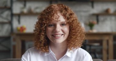 Beyaz elbiseler giyen, oturma odasında kameraya bakan kızıl saçlı neşeli kadının portresi. Evde tek başına poz veren gülümseyen öğrenci kız. İçerideki kendine güvenen kızıl saçlı genç bayanın vesikalığı.