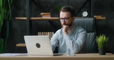 Çok çalışan iş adamının işte stresi var, modern işyerinde oturuyor. İç mekanda dizüstü bilgisayarda çalışırken bitap düşen üzgün bir erkek yönetici..