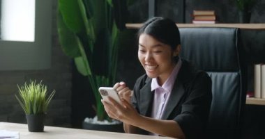 Asyalı bir kadın masa başında oturmuş akıllı telefonuyla bankadan mesaj alıyor. İnanılmaz mutlu. İş kadını evet diyor. Çok heyecanlı bir jest yaptım. Başarı, işe alınmak, piyango parası kazanmak.