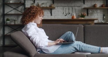 Laptop ekranına bakıp evdeki kanepede otururken kötü mesaj okuyan üzgün genç bir kadının yan görüntüsü. Mutsuz, depresyondaki genç bir kadın bilgisayar ekranına bakıyor. İnternet bahis kaybı tepkisi.