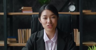 Gülümseyen Asyalı genç kadın blogger vlogger modern ofiste oturup kameraya bakarak konuşuyor. Video konferansı yapıyor, yaşam tarzı blogu yazıyor, ev konseptinde video sohbet yapıyor, webcam görüntüsü yapıyor.