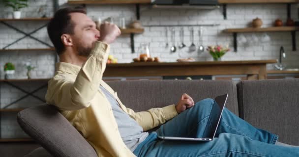 Mutlu genç adam başarıyı kutluyor online bahsi kazanıyor ve EVET hareketi gösteriyor. Şanslı erkek serbest yazar internette harika haberler okuyor. Evdeki rahat koltukta dinlenirken dizüstü bilgisayar kullanıyor.. — Stok video