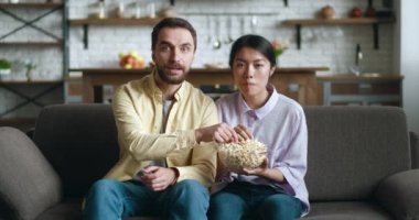 TV 'de patlamış mısırlı komedi filmi izleyen gençler evdeki koltukta oturuyorlar. Gülen çift evde birlikte komik videolar izliyor.