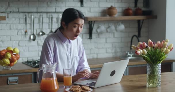 Ładna azjatycka kobieta czyta e-maile na laptopie nie może uwierzyć w szczęście, wyglądając podekscytowany zaskoczony, czuje się bardzo szczęśliwy. Młoda kobieta zwycięzca aukcji on-line świętować monetarną koncepcję zwycięstwa — Wideo stockowe