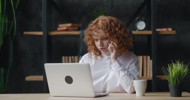 Heureuse jeune femme d'affaires professionnelle parlant au téléphone à l'aide d'un ordinateur portable assis au bureau, heureuse étudiante passer un appel mobile tout en travaillant à l'ordinateur sur le lieu de travail moderne — Video