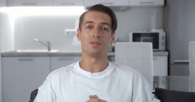 Webcam görüntüsü, gülümseyen genç adamın kamerayla konuşması evde otururken çevrimiçi video konferans görüşmesi yapması.