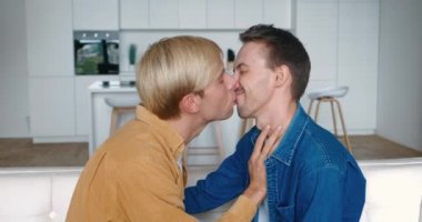 Birbirini öpen iki mutlu gay çiftin portresi evdeki kanepede otururken kafa sallıyor. LGBT İlişkisi