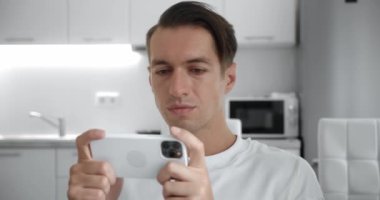 Akıllı telefonuyla oynayan genç bir adam heyecan verici mobil uygulaması. Oturma odasında rahat bir kanepede otururken yumruğunu sıkarak bir yarış oyunu kazanıyor..