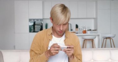 Genç adam evdeki oturma odasında kanepede otururken akıllı telefonuyla uygulama oyunu oynuyor. Mobil uygulama çalarken kaybetme kavramı