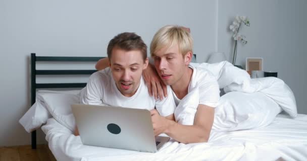 Дві пари чоловіків-геїв використовують ноутбук для відеодзвінків, розмовляючи з друзями. Два ЛГБТ-чоловіки, які мають відеозізнання, відпочиваючи на ліжку в спальні. — стокове відео