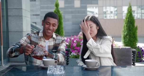 Handsome African American guy resting with his girlfriend in lounge cafe , pouring hot tea into cups and spending precious romantic moments with his girlfriend while talking together at romantic date — Stock Video