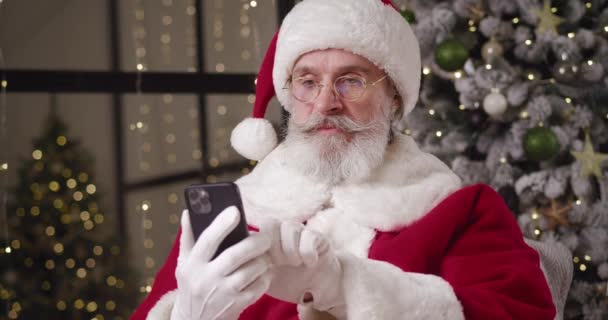 Όμορφος είδος Santa Claus περιήγηση ιστοσελίδες, κτύπημα, σερφάρισμα στο διαδίκτυο, χρησιμοποιώντας smartphones και χαρά, χαμογελώντας, σφίγγοντας γροθιές ανάγνωση μεγάλη είδηση για το σύγχρονο smartphone του. Άγιος Βασίλης online — Αρχείο Βίντεο