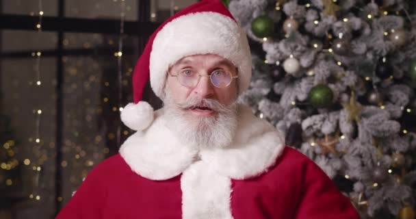 Main focus on emotions and facial expressions of a cheerful elderly bearded European man in Santa Claus carnival costume, expressing astonishment and surprise looking through his lowered goggles — Stock Video