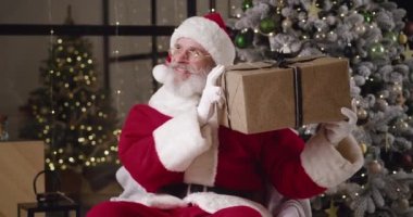 Noel Baba gibi giyinmiş olgun bir adam evinde süslenmiş Noel ağacına karşı koltuğa oturur ve Noel hediyesini kulağına getirir, orada yatanları hatırlayarak sallar.