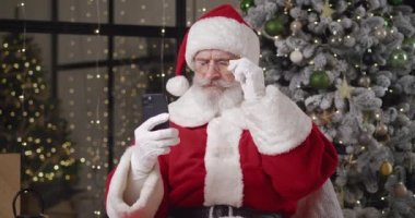 Düşüncelere dalmış yaşlı bir Noel Baba portresi akıllı telefonundaki mesajı düşük gözlükleriyle okur, olumsuz bir kararla başını sallar, bir çocuğun dileğini yerine getiremez..