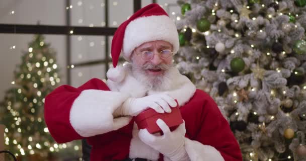 Санта-Клаус открывает волшебную светящуюся подарочную коробку и смотрит внутрь, яркий свет светит из коробки. С Новым годом и Рождеством. — стоковое видео
