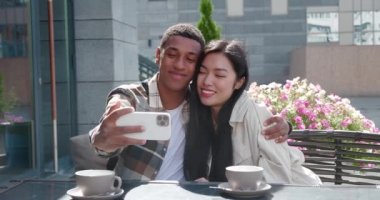 Yakışıklı, Afro-Amerikan bir adam cep telefonunu uzatmış, güzel kız arkadaşına sarılmış, onu öpmüş ve kafeterya terasında dinlenirken selfie çekmiş.