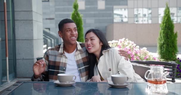 Attractive happy loving couple talking, enjoying togetherness, chilling sitting close to each other at the table while resting in the terrace of a summer cafeteria, at romantic date on warm sunny day — Stock Video