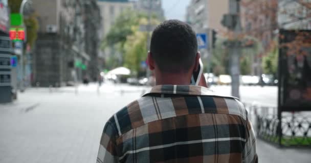 Πίσω όψη του Αφροαμερικανού νεαρού που μιλάει στο τηλέφωνο περπατώντας στους δρόμους της πόλης — Αρχείο Βίντεο