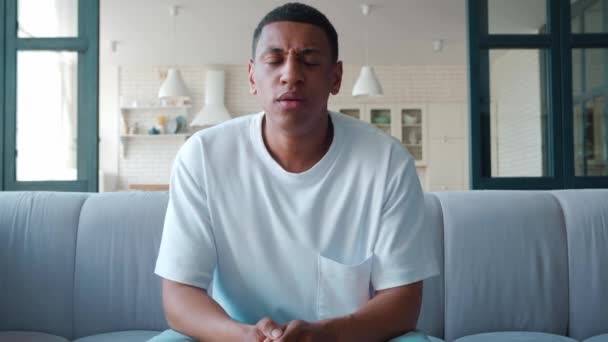 Depressed young african american guy, handsome upset mixed race man sitting on couch looking at screen, feeling desperate, frustrated, shaking his head to the sides and looking down — Video Stock