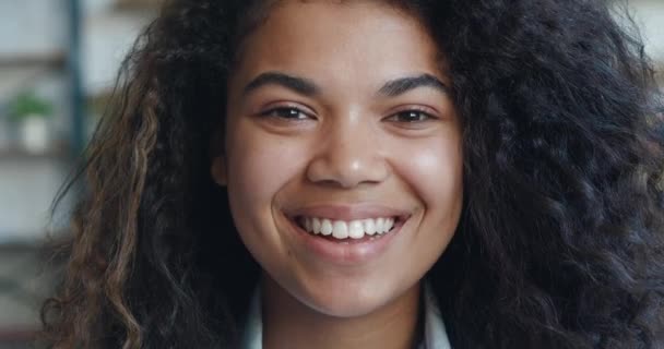 Cheerful african american woman looking at camera laughing with dental smile. Beautiful smiling young female 20 pretty face looking at camera posing alone at home, Close-up face portrait macro shot — Stockvideo
