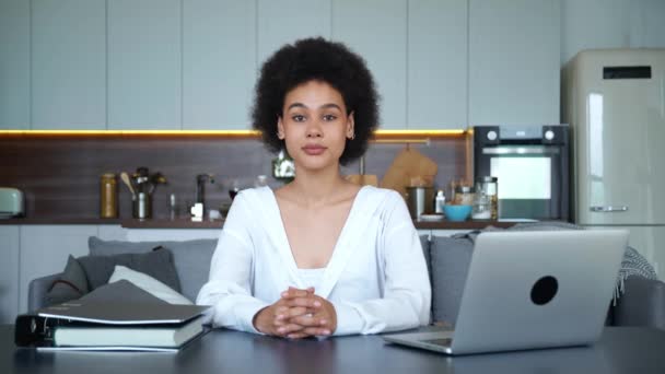 Magabiztos portré afro-amerikai fiatal szabadúszó nő dolgozik otthon ül az asztalnál a laptop és dokumentumok nézi a kamera és örül mosolygós fogas mosoly a konyhában háttér — Stock videók