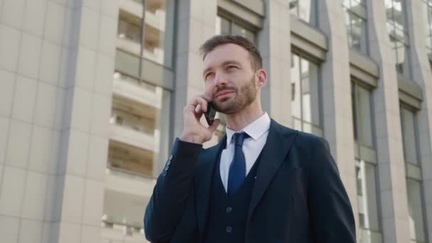 Портрет впевненого бізнесмена в класичному костюмі, який розмовляє по телефону на відкритому повітрі в діловому районі. Молодий бізнесмен має ділову розмову . — стокове відео
