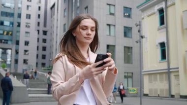 Şehir caddesinde yürürken cep telefonuyla yazan kendine güvenen iş kadınının portresi. İşe giderken akıllı telefon kullanarak kadın yöneticiyi kapat. Sabit çekim.
