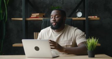 Mutlu Afro-Amerikan adam ofis masasında otururken dizüstü bilgisayarla video görüşmesi yapıyor. Teknoloji ve iletişim konsepti