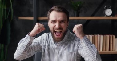 Evet, kazanan jest. İnanılmaz Avrupalı iş adamı zaferi kutluyor. Kazanıp ellerini kaldırıyor, kameraya şaşırıyor, modern ofiste oturuyor. Zafer konsepti.