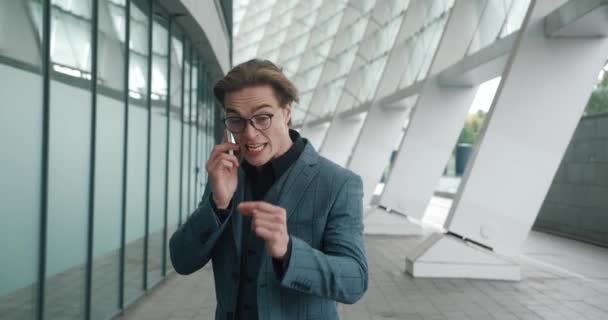 Angry businessman in formal suit emotionally talking by mobile phone while standing outside at downtown near office buildings. Serious businessman having aggressive negotiating by phone — Video Stock