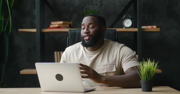 Hombre afroamericano feliz tener haciendo videollamadas usando computadora portátil mientras está sentado en el escritorio de la oficina en casa. Concepto de tecnología y comunicación — Vídeo de stock