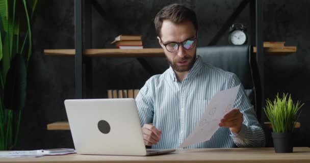 眼鏡のビジネスマンは、ノートパソコンで会議ビデオ通話を行うことを確認します。男性プロのマネージャーは、オフィスでコンピュータ上のビジネスミーティングインタビューをウェブカメラの距離を持っています. — ストック動画