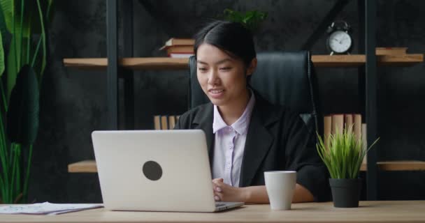 Ázsiai üzletasszony video chat laptoppal az irodában. Női menedzser beszél és nézi laptop képernyőn, miközben ül az asztalnál. Webkamera webinar koncepció — Stock videók