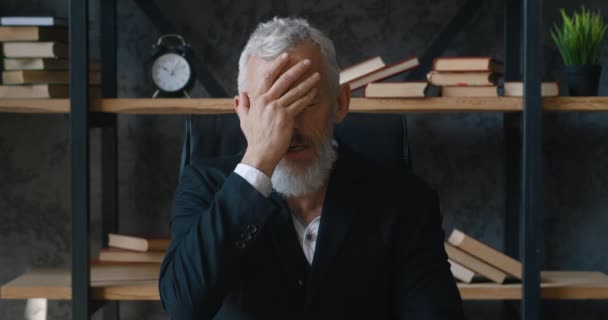 Shocked mature businessman looks at camera and covers his face with his hands in surprise at the terrible news. Frightened business man reacting to bad news while sitting indoors in a modern office. — Stock Video