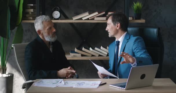 Dva podnikatelé, kteří používají notebook a vedou diskuzi v moderní kanceláři. Starší muži obchodní kolegové diskutovat obchodní diagramy, firemní grafy poradenství na setkání kanceláře. — Stock video