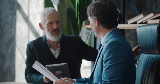 Two mature businessmen discussing business growth in modern office while sitting at desk. Man ceo talking with colleague about deal while meeting indoors — Stockvideo